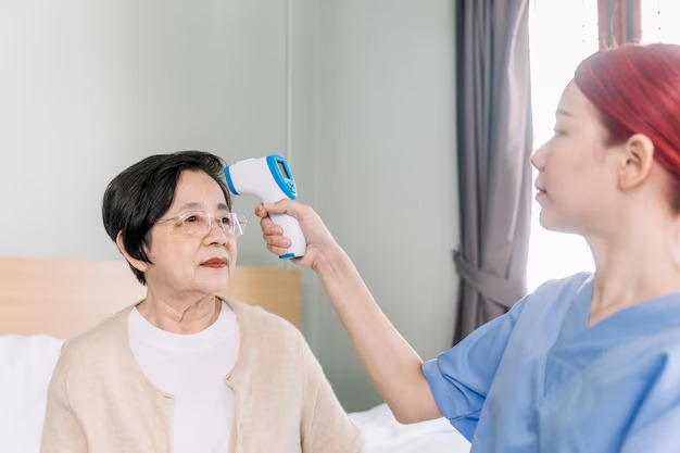 A caregiver taking an elderly woman’s temperature using a contact thermometer
